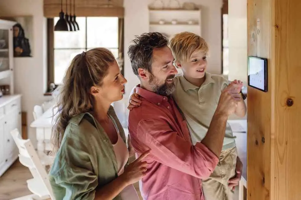 Familie mit Mutter, Vater und kleinem Sohn schaut gemeinsam lächelnd auf ein Smartphone im Wohnzimmer.