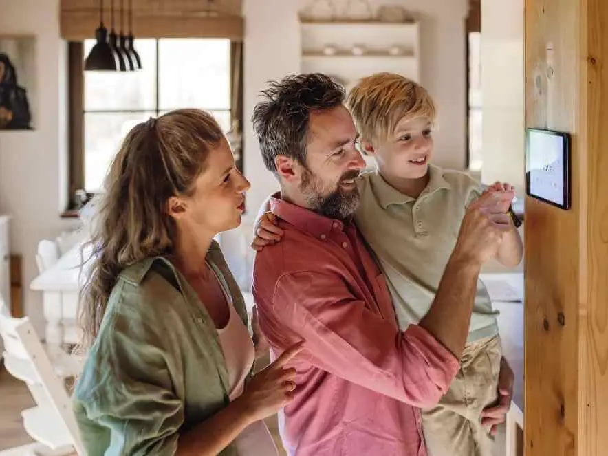 Familie mit Mutter, Vater und kleinem Sohn schaut gemeinsam lächelnd auf ein Smartphone im Wohnzimmer.