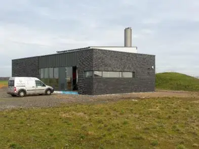 Modernes, freistehendes Technikgebäude mit dunkler Fassade in ländlicher Umgebung, davor steht ein Servicefahrzeug.